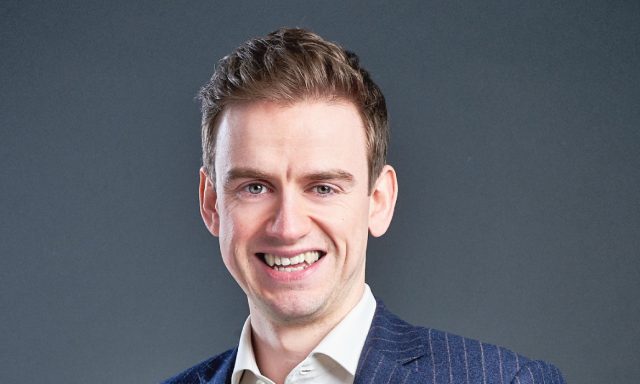 Man Jonathan Bloor smiling in front of grey screen