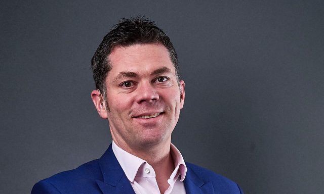 Paul Campbell smiling infront of grey screen