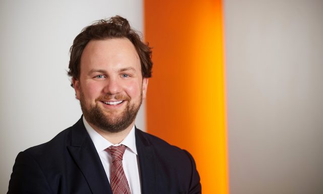 Man Zack Simons smiling in front of orange and grey screen