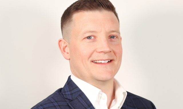 White man smiling into the camera in suit and shirt