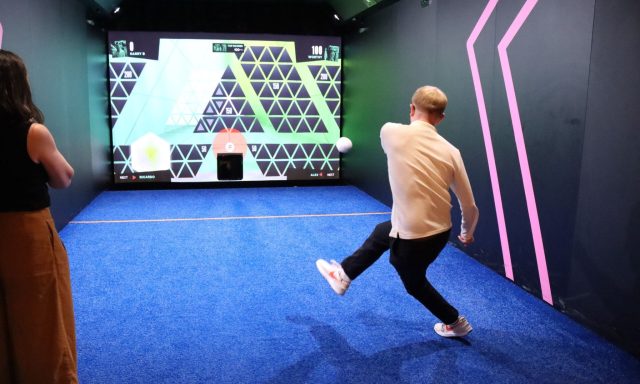 Image shows man kicking ball at a screen showing targets